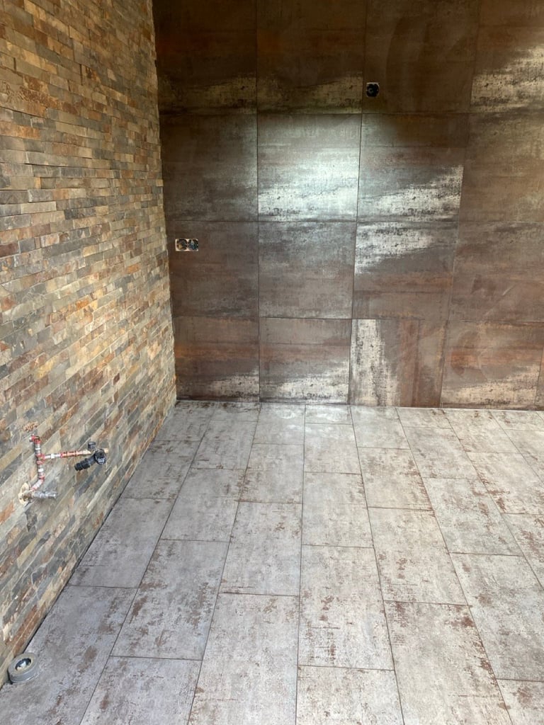 Empty bathroom under construction with exposed brick wall, tiled floor, and glass shower enclosure framework