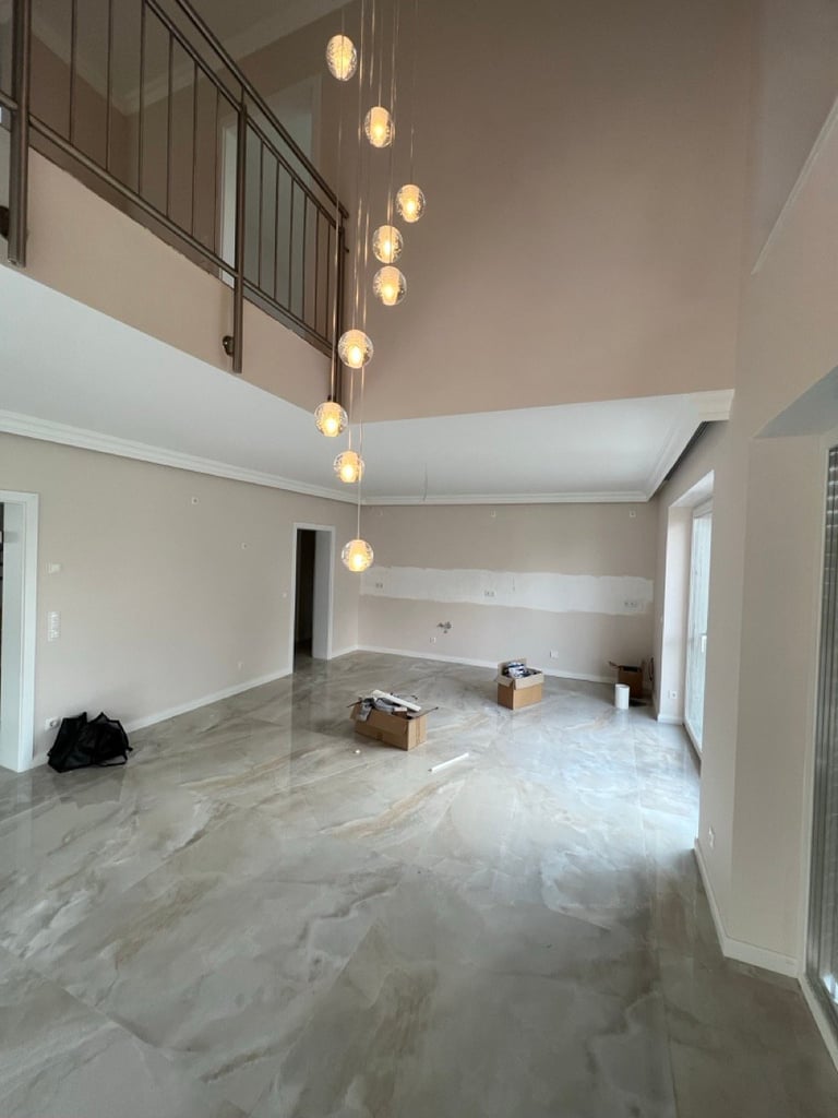 Modern open-concept interior with hanging pendant lights, marble flooring, white walls, and mezzanine level