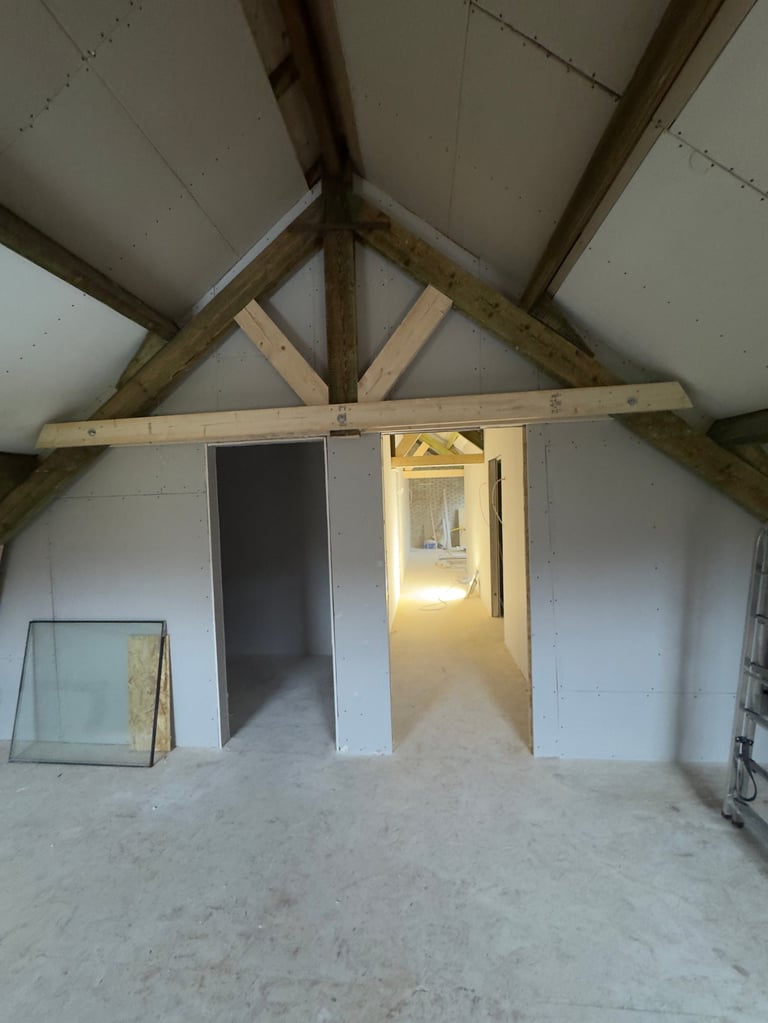 Unfinished attic interior with exposed wooden beams, drywall partitions, open doorway, and concrete floor during construction