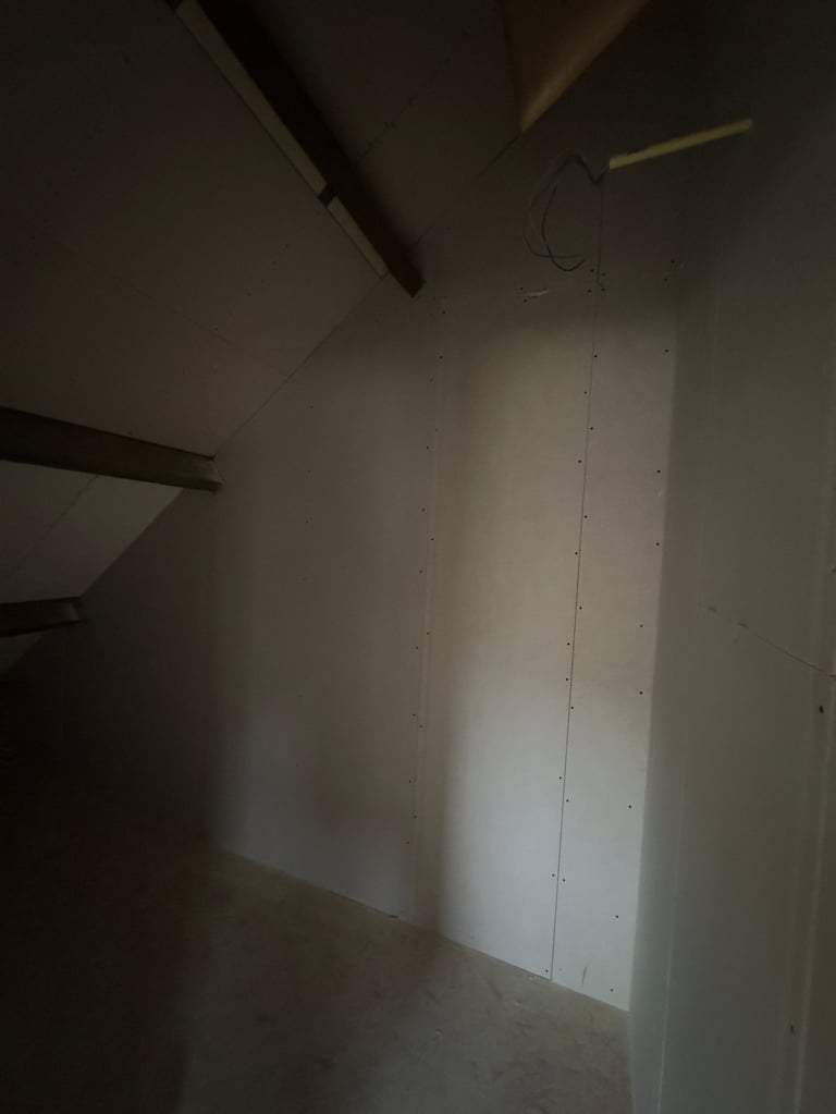 Interior view of an unfinished room with white drywall, exposed ceiling beams, and a vertical electrical outlet box on the wall