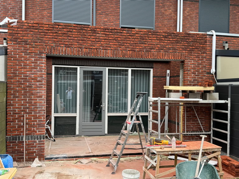 Home renovation in progress with ladder and work platforms outside brick house patio doors