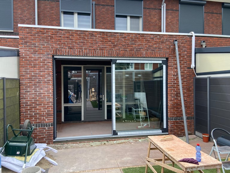 Modern black framed glass patio doors in red brick building with concrete patio and construction materials