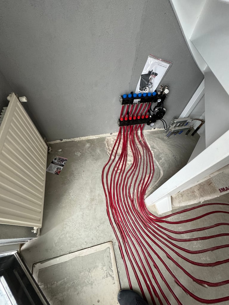 Red electrical wires organized with blue clips on concrete floor in an unfinished room with white radiator and fixtures