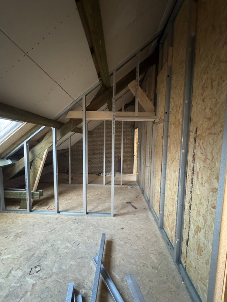Interior of attic space under construction with wooden frame walls, metal studs, and exposed roof beams