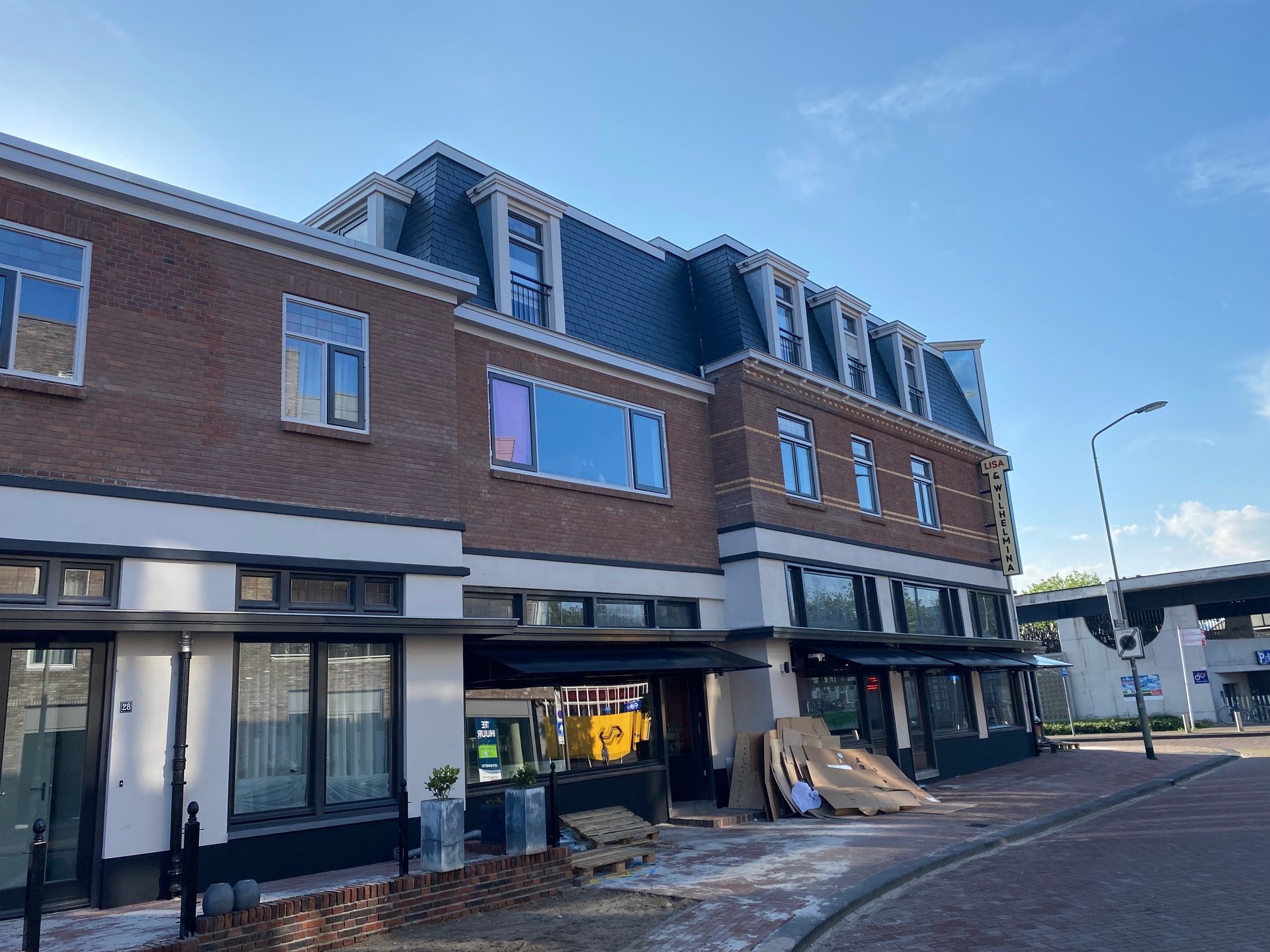 Modern brick building with mansard roof, ground-floor retail space, and residential apartments above in a commercial area