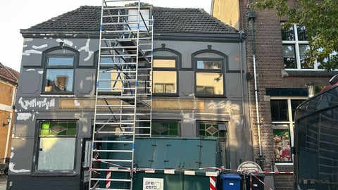 Donkergrijs bedrijfspand met steigers en groene deuren