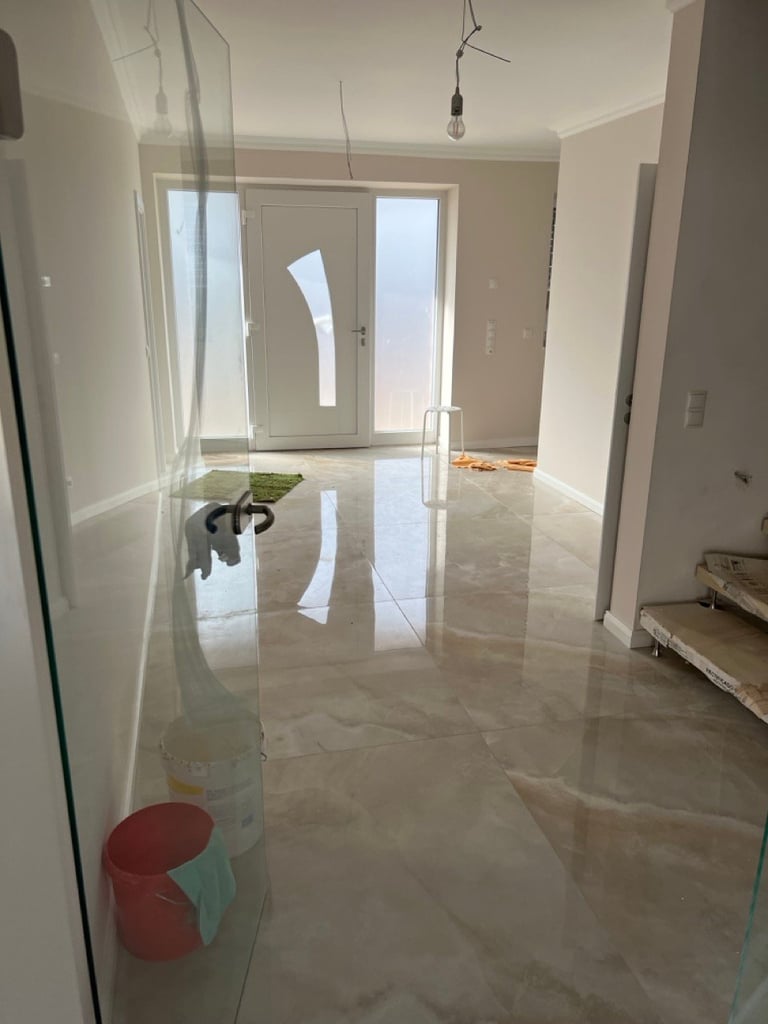 Empty room under construction with polished concrete floor, white walls, glass doors, and protective plastic sheeting