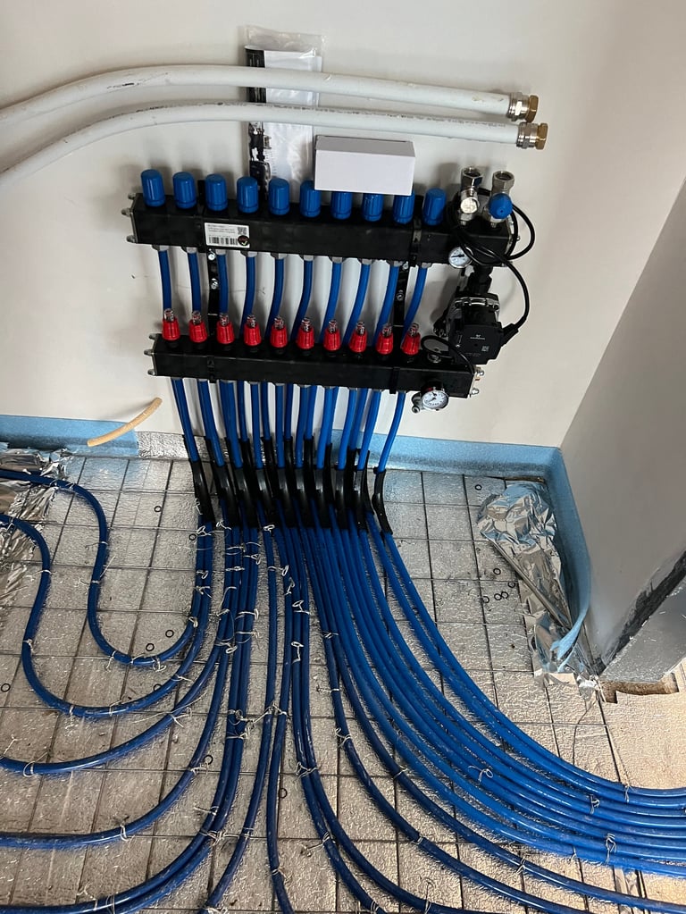 Organized plumbing manifold system with blue and red valve connections and multiple hoses running downward on white wall