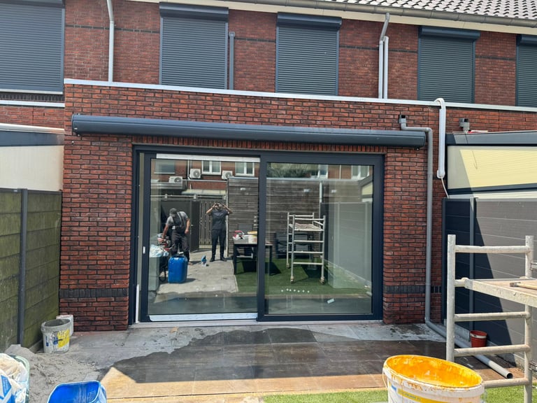 Modern glass sliding patio doors on brick residential home with wet concrete patio and construction materials nearby