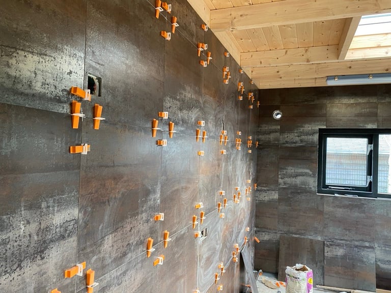Construction bathroom with dark tile walls, orange spacers on tiles, skylight, and window in unfinished interior
