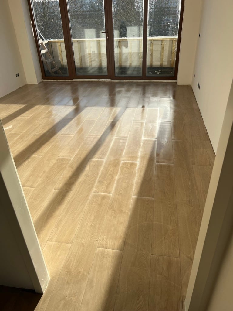 Empty room with light wood tile flooring and large glass doors leading to a patio, sunlight streaming across the floor