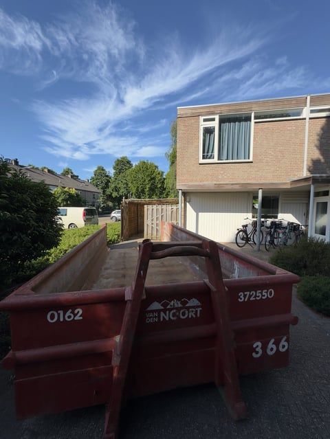 Red industrial cargo trailer parked on a street in front of a brick residential house