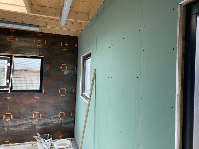 Bathroom renovation in progress with drywall installation, exposed framing, and dark tile work on walls