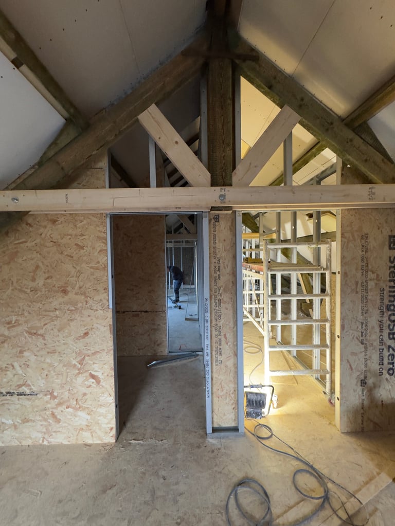 Interior of new construction home showing exposed wooden roof beams, OSB walls, doorways, and wooden framing studs under construction