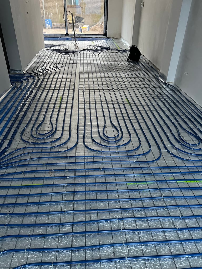 Underfloor heating system with blue tubing installed on concrete floor in empty room with window and door